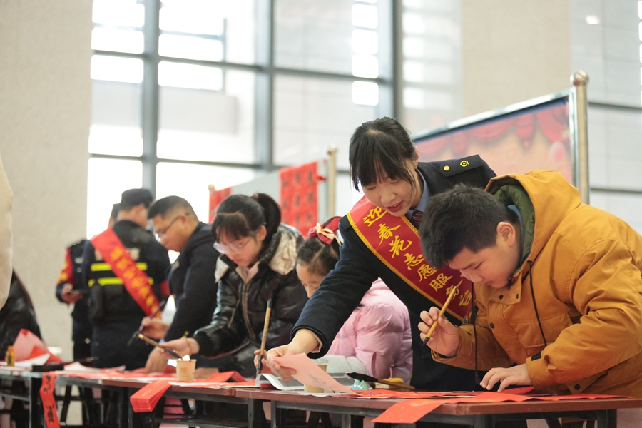 1月26日，鐵路迎春花志愿服務(wù)臺(tái)工作人員協(xié)助小旅客手寫(xiě)春聯(lián)送福，傳遞滿(mǎn)滿(mǎn)年味。 張海根攝